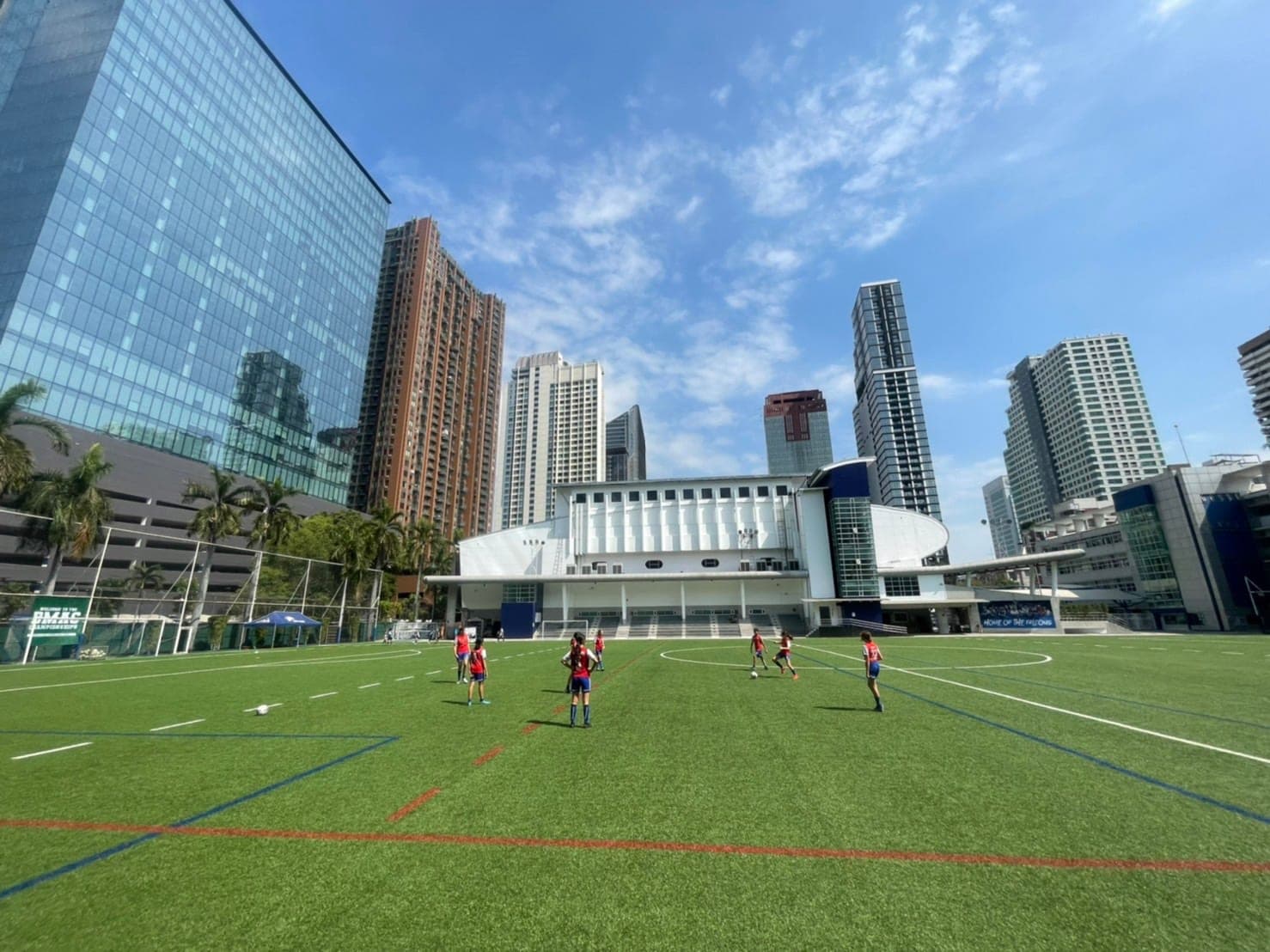 Lions FC players spread across a full-size artificial pitch, with Bangkok tower blocks rising behind the stand
