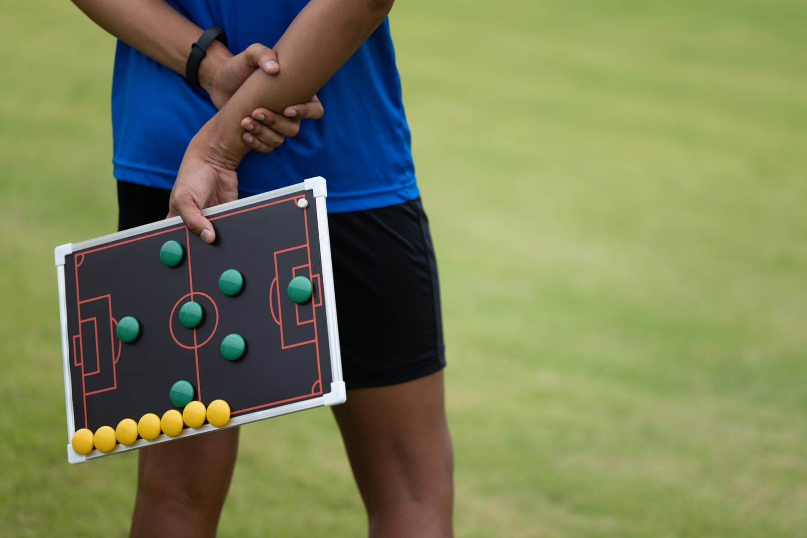 A coach standing on the grass with a tactics board held behind his back, the magnets laid out in a formation