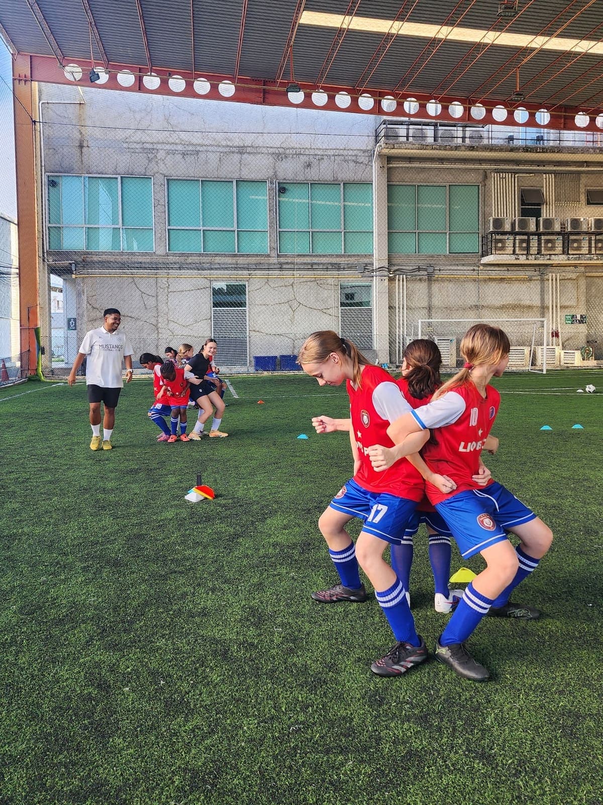 Игроки Lions FC смеются на тренировке, позади них тренер и конусы