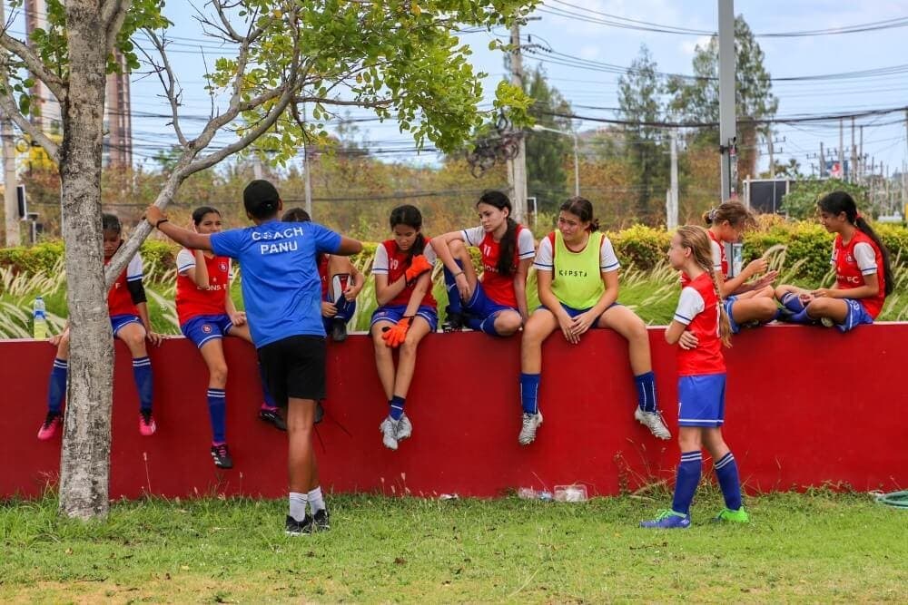 Players sitting along a low wall beside the pitch between games