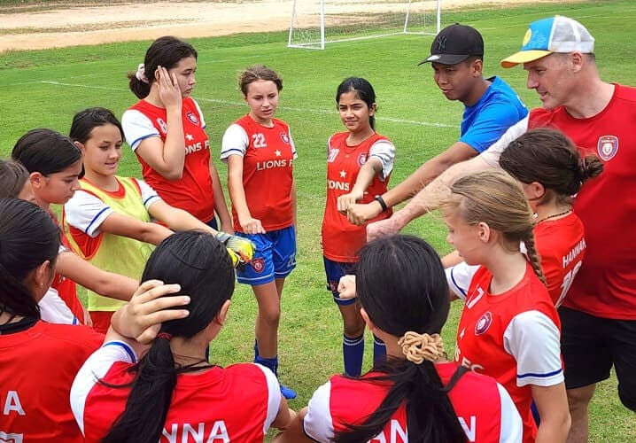 The team in a huddle with their coaches, hands together in the middle