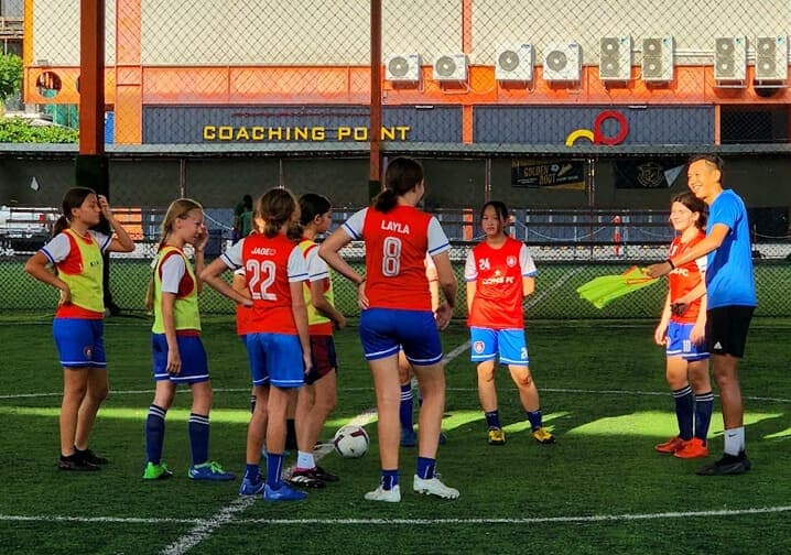 Players gathered around a ball with their coach during a training session