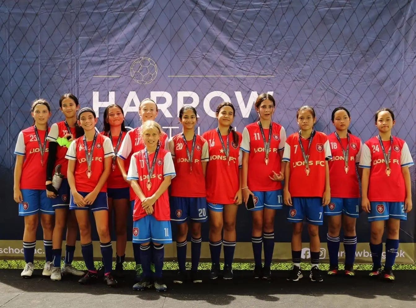 The squad with their medals in front of the tournament board at Harrow