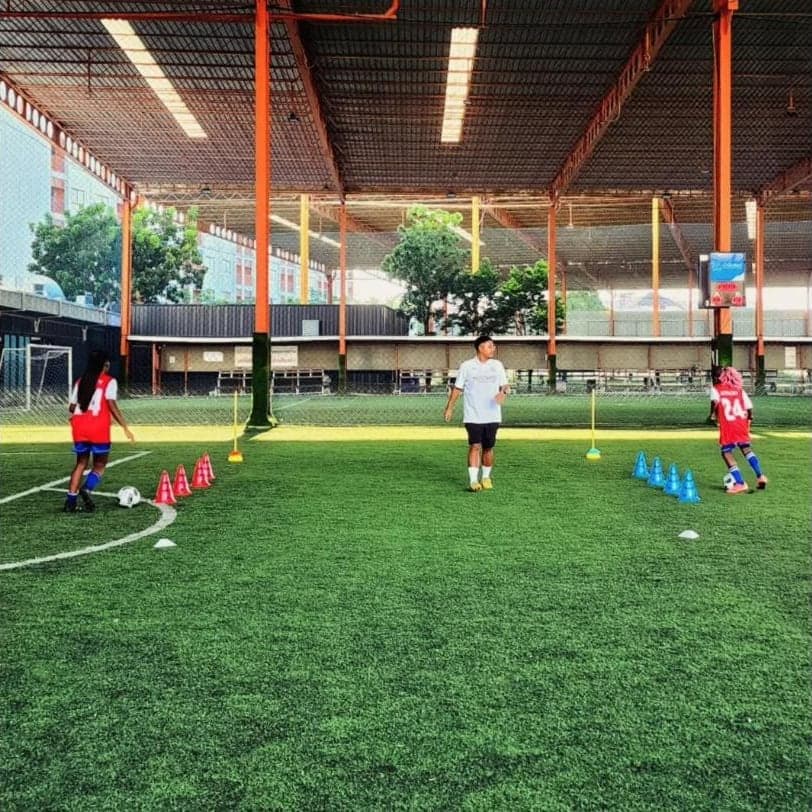 A Lions FC session in progress on the covered pitch at SoccerPro Bangna, with cones laid out and a coach running the drill