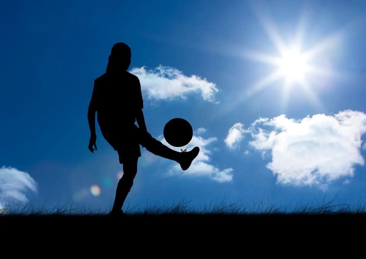 A player silhouetted against the sky with the ball at her feet